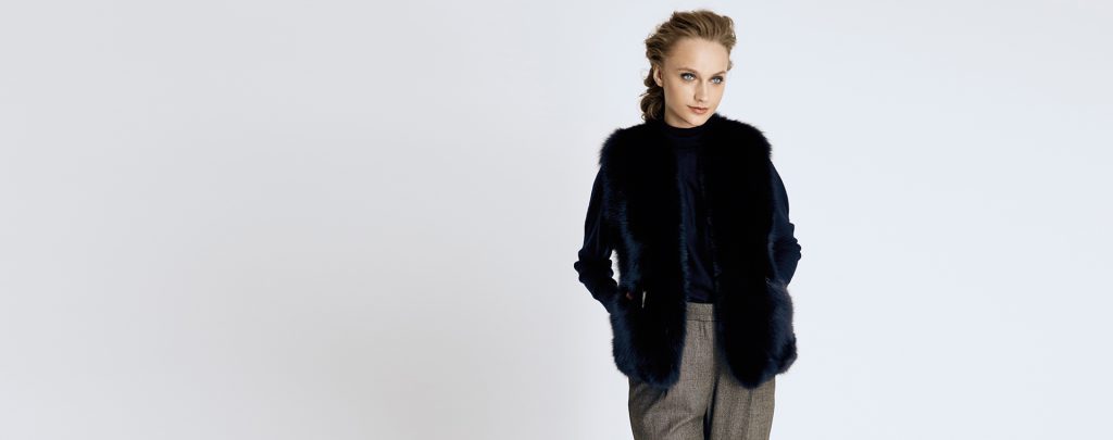 A stylish woman wearing a black women fur vest over a monochrome outfit.